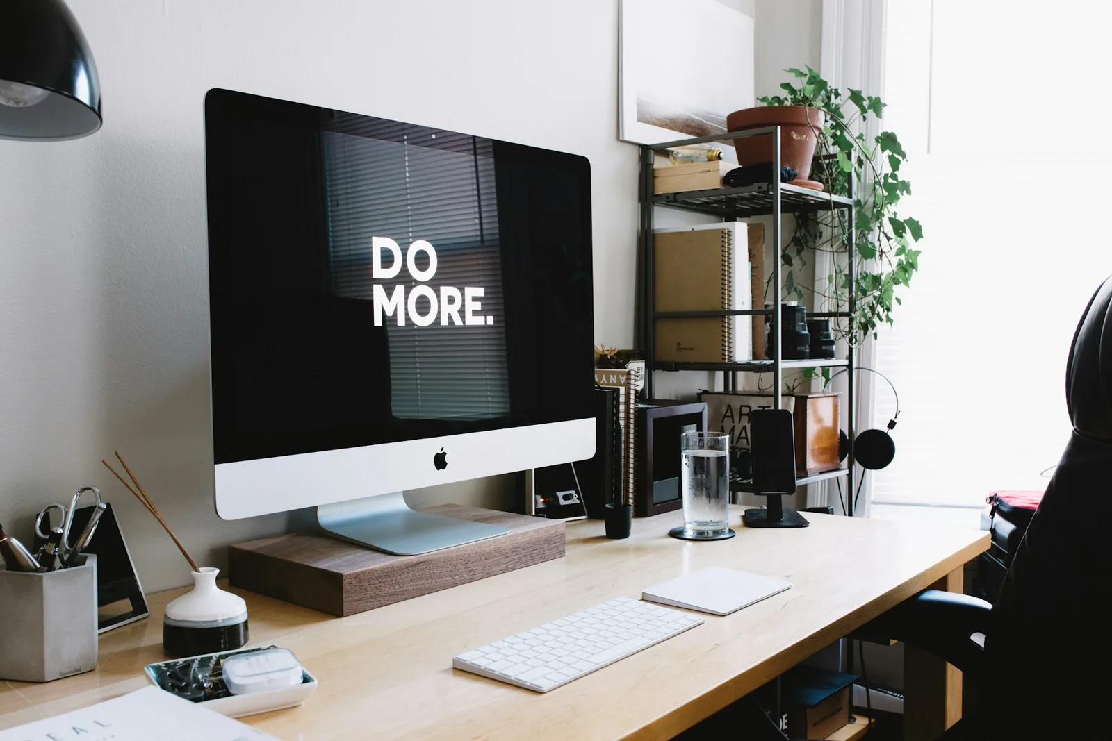 An iMac, keyboard and plants on a wooden desk.